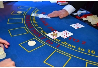 Närbild på ett blått blackjack-bord. En dealer håller på att dela ut kort till spelarna vid bordet.